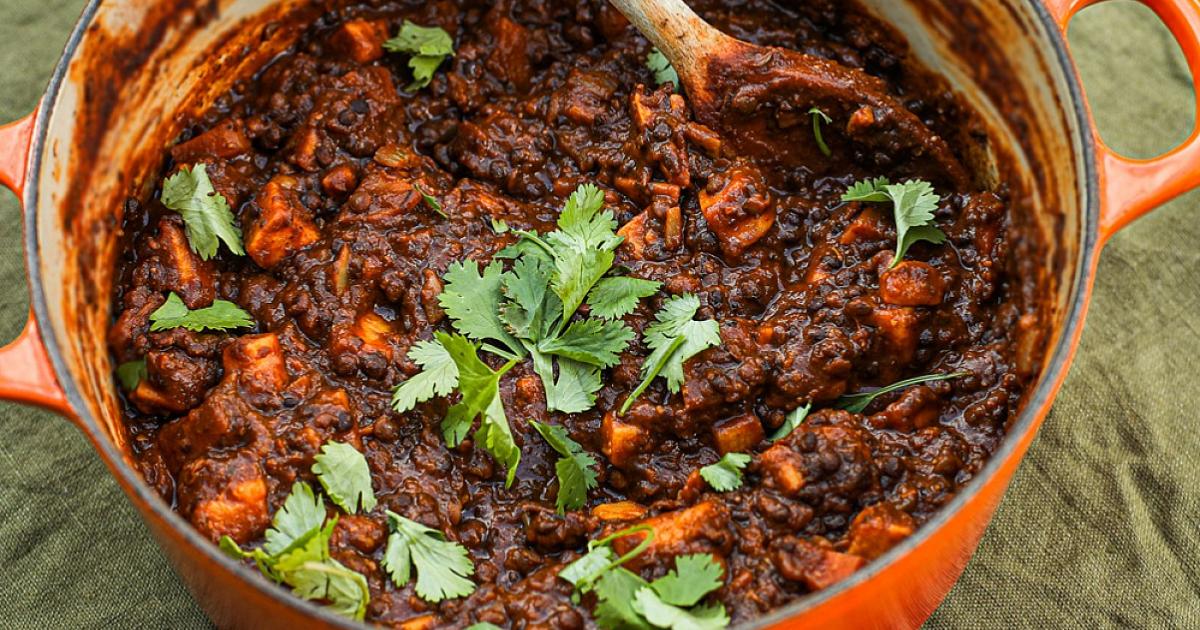 no meat beluga lentil stew scattered with fresh herbs in red pot and wooden spoon on green table cloth