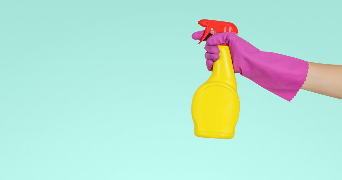 turquoise background yellow spray bottle held by pink rubber glove hand ready to spray